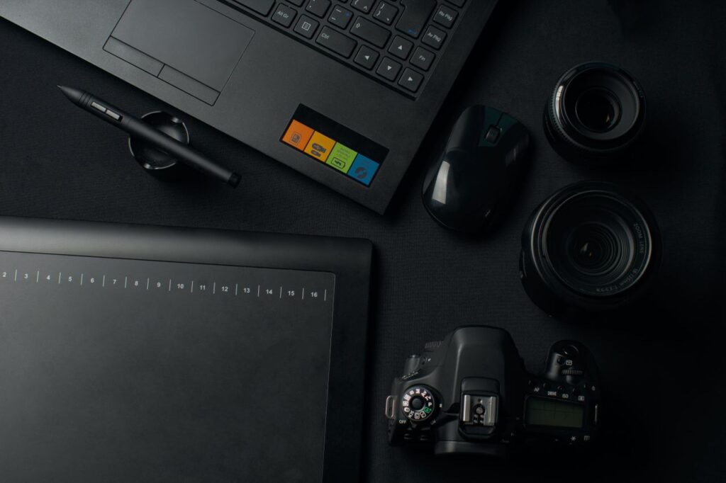 Top view of a modern workspace setup featuring a camera, laptop, graphic tablet, and lenses for photography and editing.